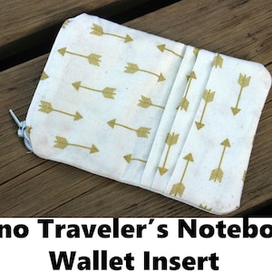 Peut inclure: Portefeuille en tissu blanc avec un motif de flèches dorées. L'insert est doté d'une fermeture à glissière et est conçu pour s'adapter à un petit carnet.