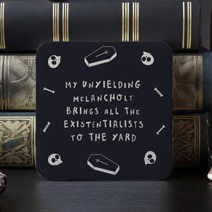 May include: Black square coaster with white text that reads "My Unyielding Melancholy Brings All The Existentialists To The Yard". The coaster is decorated with small skull and coffin graphics.