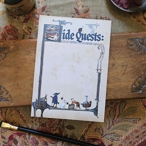 May include: A rectangular notepad with a cream-coloured page featuring the blue text "Side Quests:" at the top. The border is decorated with blue medieval-style illustrations of figures, animals, and a snail. A black pencil lies horizontally below.