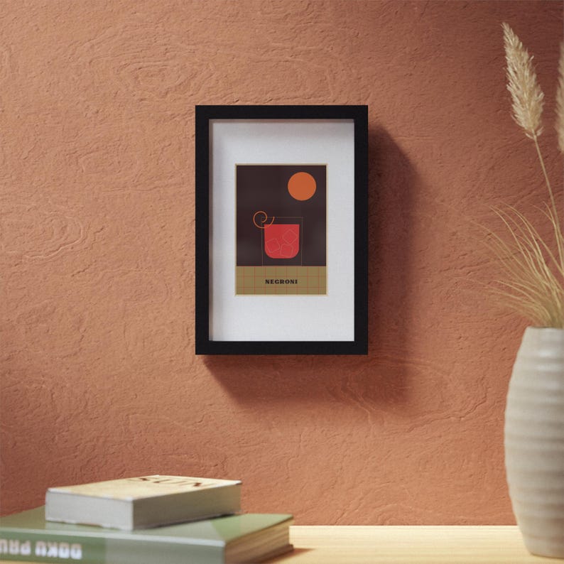 May include: A black framed print with a minimalist design of a red Negroni cocktail with a slice of orange. The text "Negroni" is printed below the cocktail.