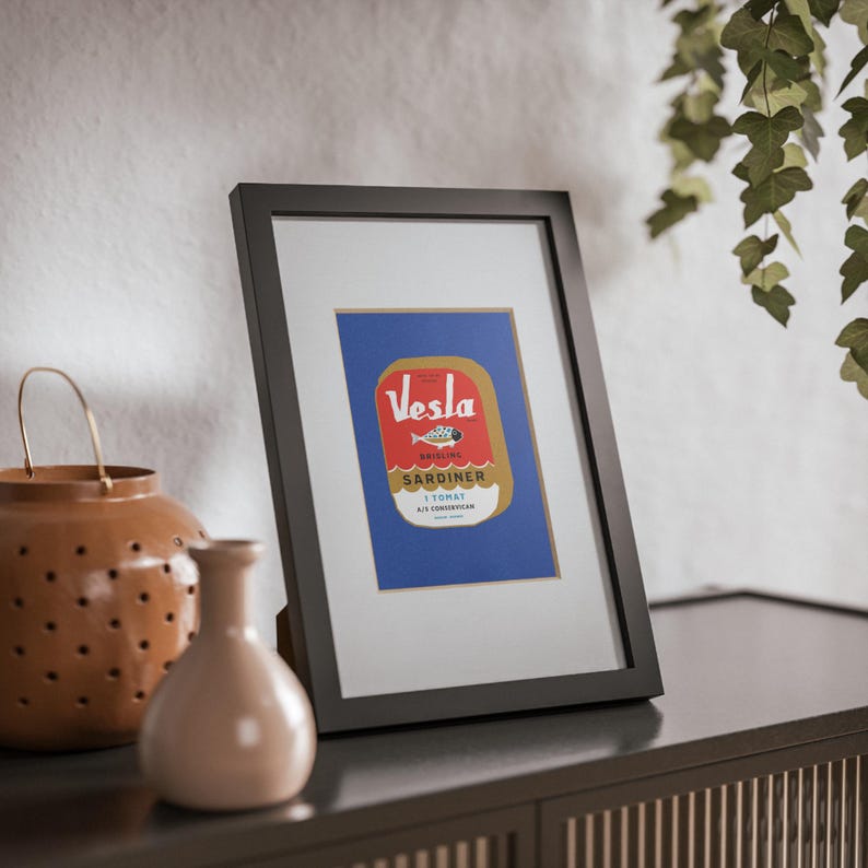 Puede incluir: Una impresi&oacute;n enmarcada de una etiqueta vintage de una lata de sardinas. La etiqueta es roja, amarilla y azul con el texto "Vesla Sardiner I Tomat" y un dibujo de un pez.