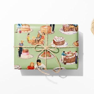 May include: A wrapped gift with a green background featuring a vintage cake design. The gift is tied with twine and a bow. Black scissors and a spool of twine are on a white surface.