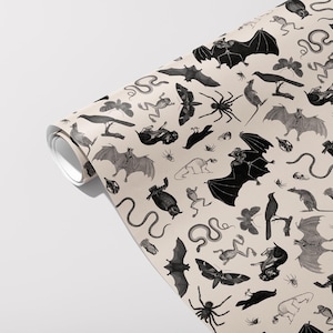 May include: Rolled wallpaper featuring a repeating pattern of black and gray bats, spiders, snakes, frogs, moths, and crows on a beige background. The design has a vintage, Halloween-themed aesthetic.