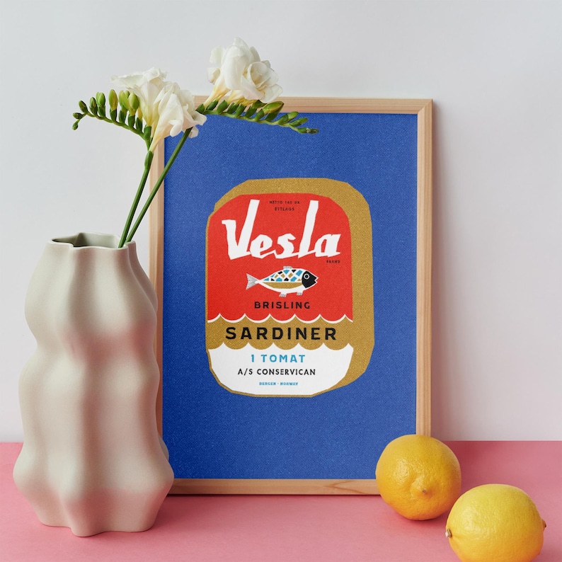 Puede incluir: Una impresi&oacute;n enmarcada de una etiqueta de lata de sardinas vintage con el texto "Vesla Brisling Sardiner 1 Tomat A/S Conservican" en rojo, azul y blanco sobre un fondo dorado. La etiqueta de la lata est&aacute; sobre un fondo azul.