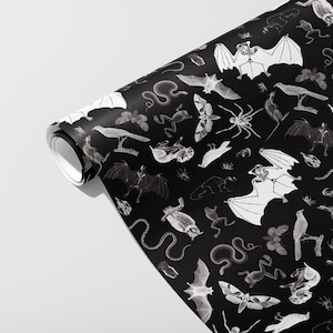May include: A roll of black wallpaper featuring a repeating pattern of white illustrations of bats, spiders, snakes, birds, and other creatures. The wallpaper is partially unrolled, revealing the pattern against a white background.