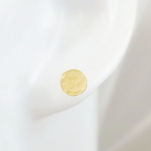 May include: A pair of gold hammered disc earrings. The earrings are small and round, with a textured surface.