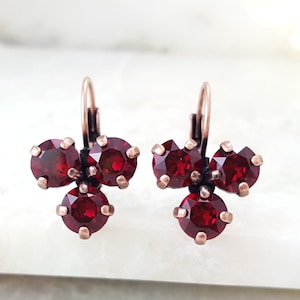 May include: A pair of red crystal earrings with a cluster of three stones on each earring. The earrings are made with a copper wire and have a hook closure.