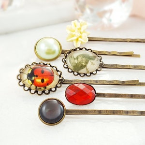 May include: Set of six gold hair clips with various decorative accents. The accents include a ladybug, a floral design, a pearl, a red gemstone, and a black gemstone.