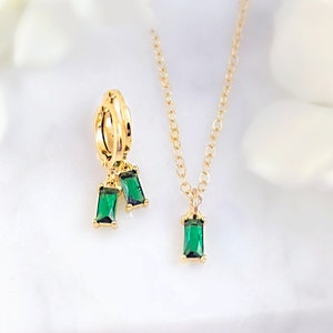 May include: Gold hoop earrings with two dangling emerald green rectangular stones. A matching gold necklace with a single emerald green rectangular stone pendant. "Get the matching necklace to have a set!" text is visible at the bottom of the image.
