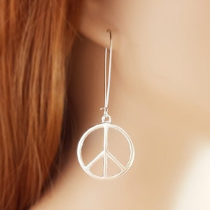May include: Silver peace sign dangle earrings. The earrings are silver and feature a peace sign charm.