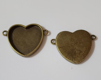 May include: Two antique bronze-colored heart-shaped pendant trays with small loops on each side for attaching to a chain or other jewelry components. One tray is empty, and the other has a textured surface.