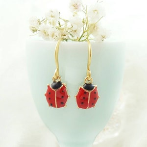 May include: A pair of gold earrings with red and black ladybug charms.