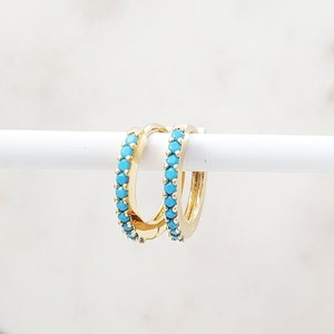 May include: A pair of gold hoop earrings with a turquoise stone accent. The earrings are small and delicate.