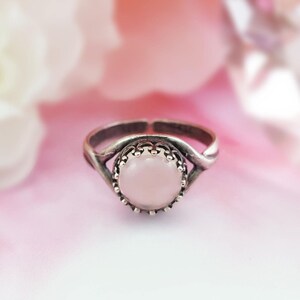 May include: A silver ring with a delicate twisted band and a round pink stone set in a crown-like bezel.