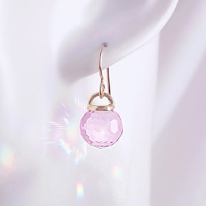 May include: A pair of delicate earrings featuring a single pink faceted gemstone on each earring. The earrings are suspended from a gold-toned wire.
