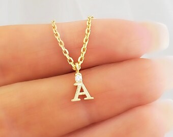 May include: A gold necklace with a small letter A pendant and a single clear stone.