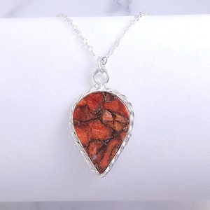 May include: A silver necklace with a teardrop-shaped pendant featuring a red and brown marbled stone.