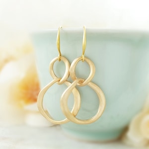 May include: Gold-toned double circle earrings with a brushed finish. The earrings have a simple, modern design.