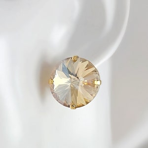 May include: A pair of gold stud earrings with a clear, faceted, round crystal in the center. The crystal has a light champagne color.