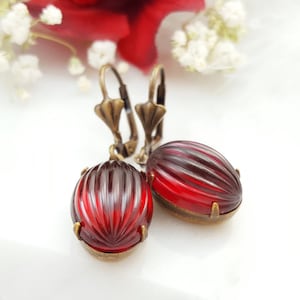 May include: A pair of red glass earrings with a ribbed texture. The earrings have a bronze-colored metal setting and a hook closure.