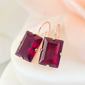 May include: A pair of rose gold earrings with rectangular red garnet stones. The earrings have a simple, elegant design.