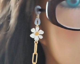 May include: A gold chain with a white daisy charm attached to it. The chain is used to hold glasses in place.