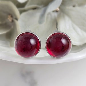 May include: A pair of silver stud earrings with round, red glass stones.