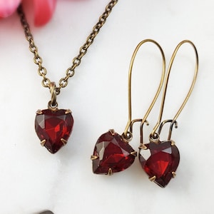 May include: A set of heart-shaped earrings and a necklace with red gemstone accents. The jewelry is made of brass and features a vintage style.