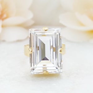 May include: A gold ring with a large, clear, rectangular emerald-cut gemstone.