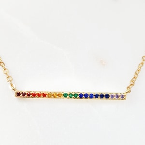 May include: A gold necklace with a thin bar pendant featuring a rainbow of colorful gemstones.