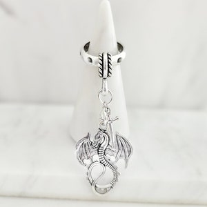 May include: Silver ring with a dragon and sword charm. The ring is adjustable and has a textured band.
