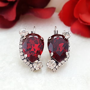 May include: A pair of silver earrings with a teardrop-shaped red crystal and smaller clear crystals.