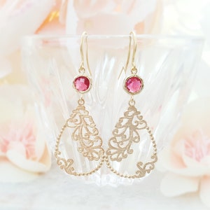 May include: Gold filigree earrings with pink gemstone drops. The earrings are delicate and intricate, with a floral design.