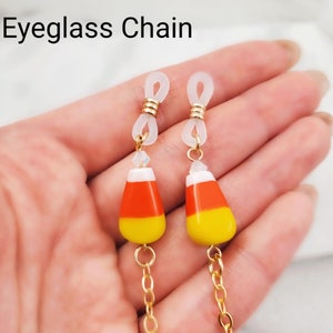 May include: Gold chain eyeglass holder with candy corn-shaped beads. The chain has clear plastic loops on each end.