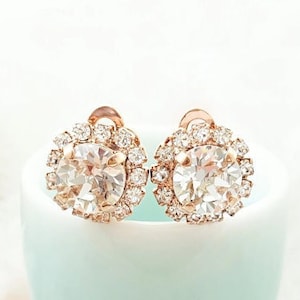 May include: A pair of rose gold earrings with a large clear crystal surrounded by smaller crystals.
