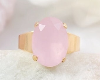 May include: A gold ring with a large oval-shaped pink gemstone. The ring is set on a white background.