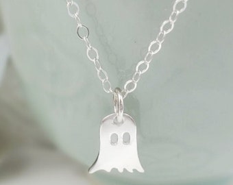 May include: A silver chain necklace with a small silver ghost charm. The ghost has two small circles for eyes.