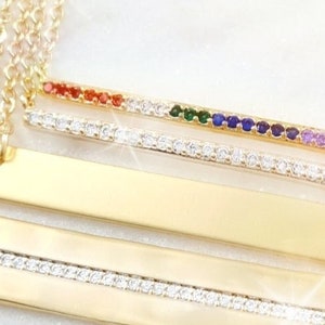 May include: Gold layered necklace with a bar pendant featuring a row of colorful gemstones and a double row of clear cubic zirconia stones.