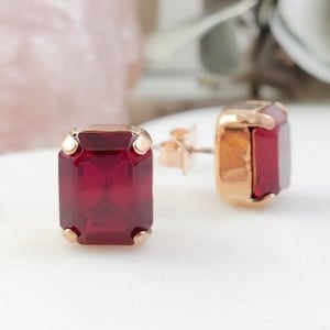 May include: A pair of rose gold stud earrings with square-shaped red gemstones.