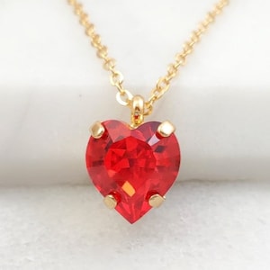 May include: A gold chain necklace with a red heart-shaped crystal pendant.
