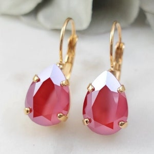 May include: A pair of gold dangle earrings with teardrop-shaped red iridescent crystals.