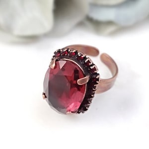 May include: A copper ring with a large, oval-shaped, red gemstone surrounded by smaller red gemstones.