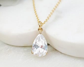 May include: A gold-toned necklace featuring a clear, pear-shaped faceted gemstone pendant. The pendant is suspended from a delicate gold-toned chain, showcasing a classic teardrop design with a polished metal setting that secures the stone.