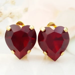 May include: A pair of gold heart-shaped earrings with red crystal stones.