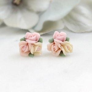 May include: A pair of delicate earrings featuring a cluster of three pink and cream roses with green leaves. The roses are made of polymer clay and have a realistic appearance.