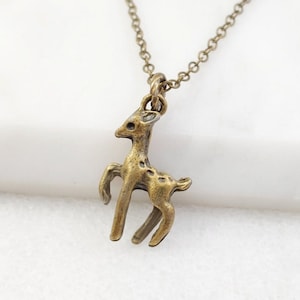 May include: A gold-toned necklace with a small, detailed deer pendant. The deer is standing on all four legs with its head held high.