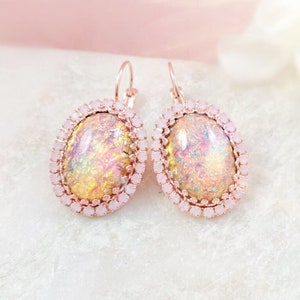 May include: A pair of rose gold earrings with oval-shaped iridescent opal stones set in a halo of small pink rhinestones.