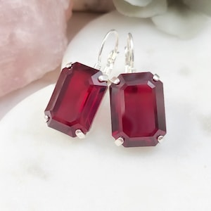 May include: A pair of silver earrings with red emerald-cut crystal stones.