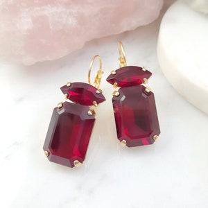 May include: A pair of gold earrings with two large, faceted, red gemstones. The earrings have a dangling design with a smaller, red gemstone above the larger one.