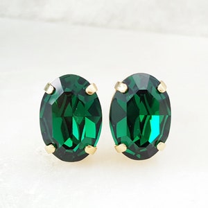 May include: A pair of oval-shaped emerald green stud earrings with gold settings.